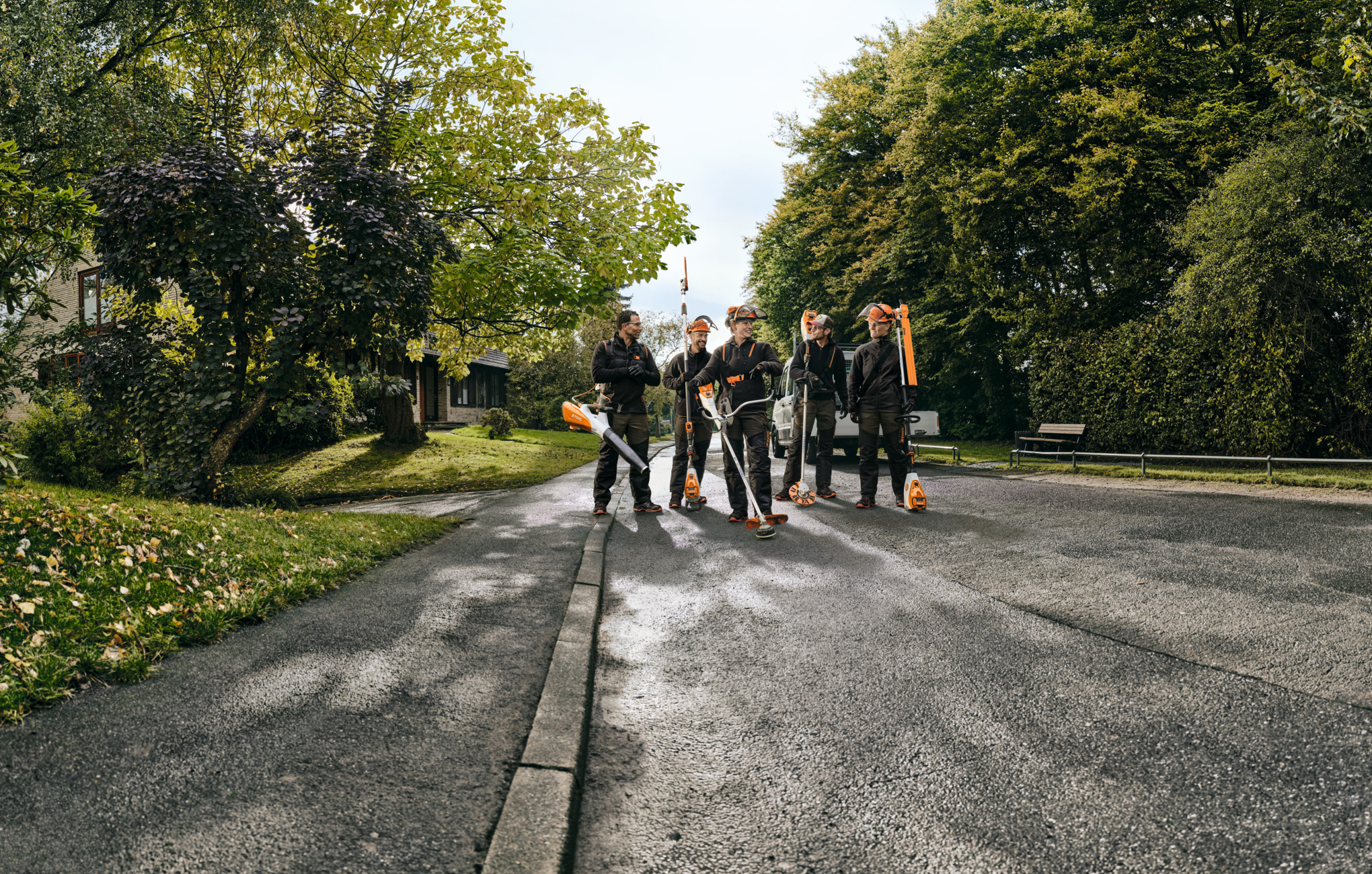 Five STIHL professionals walking along a road holding cordless power tools