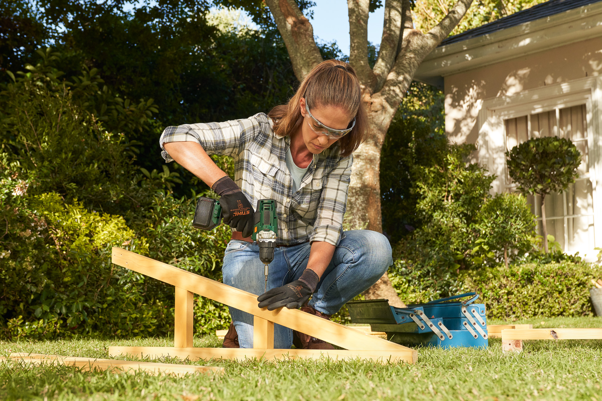 A person wearing STIHL protective gloves using a cordless drill on a wooden beam