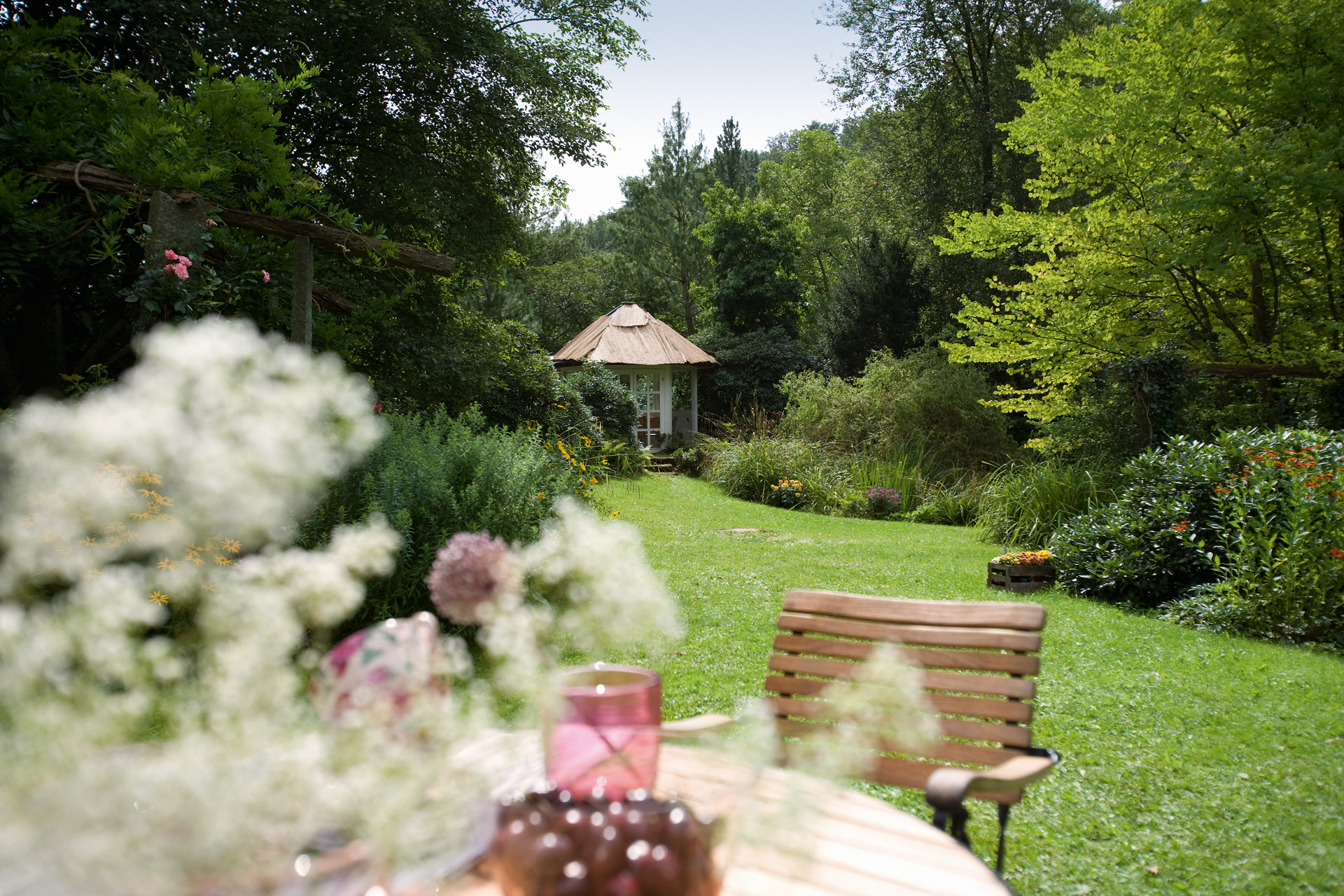 A long garden with a green lawn, a chair in the foreground and a garden room in the distance