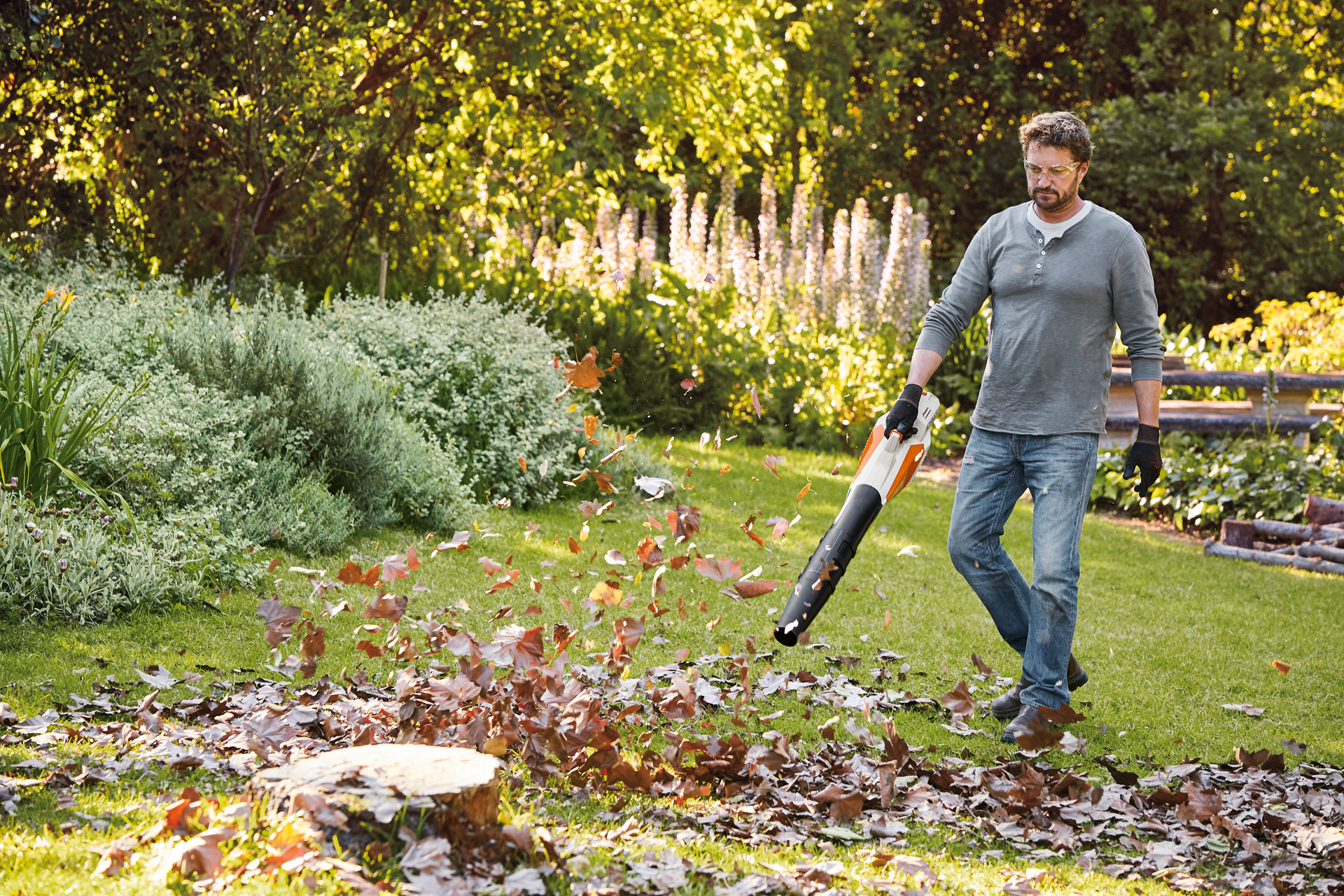 Un homme souffle des feuilles dans un jardin à l’aide d’un souffleur à batterie STIHL BGA 57