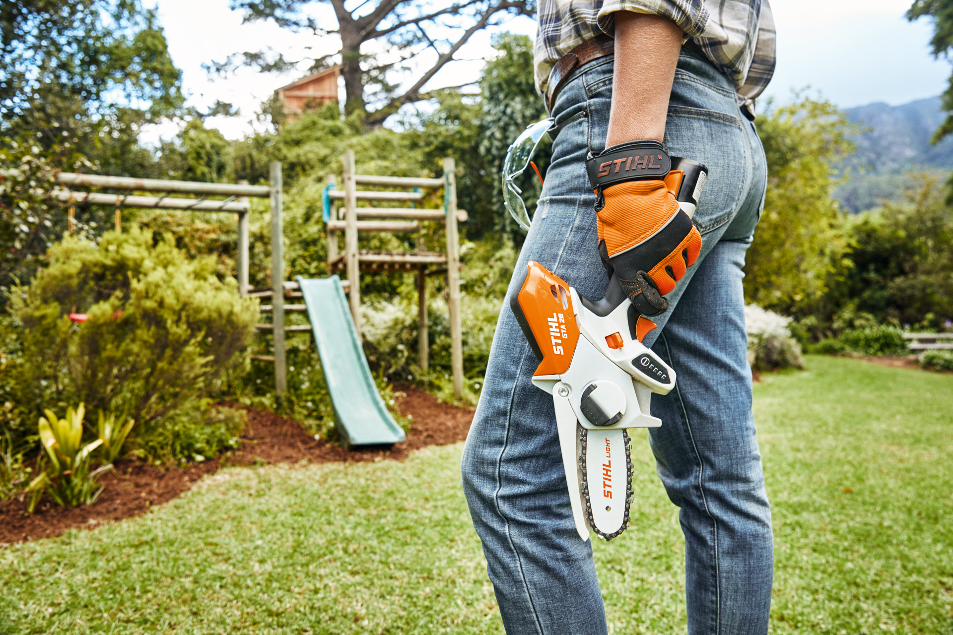 Une personne équipée d’une scie de jardin à batterie STIHL GTA26 devant un toboggan dans le jardin