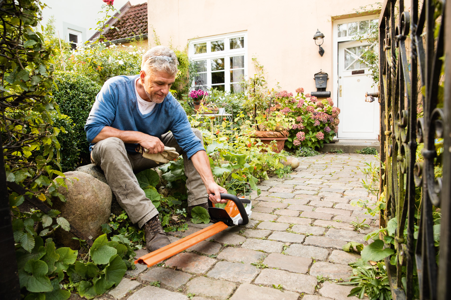 A man with an AI Series STIHL HSA 45 battery hedge trimmer in front of a house