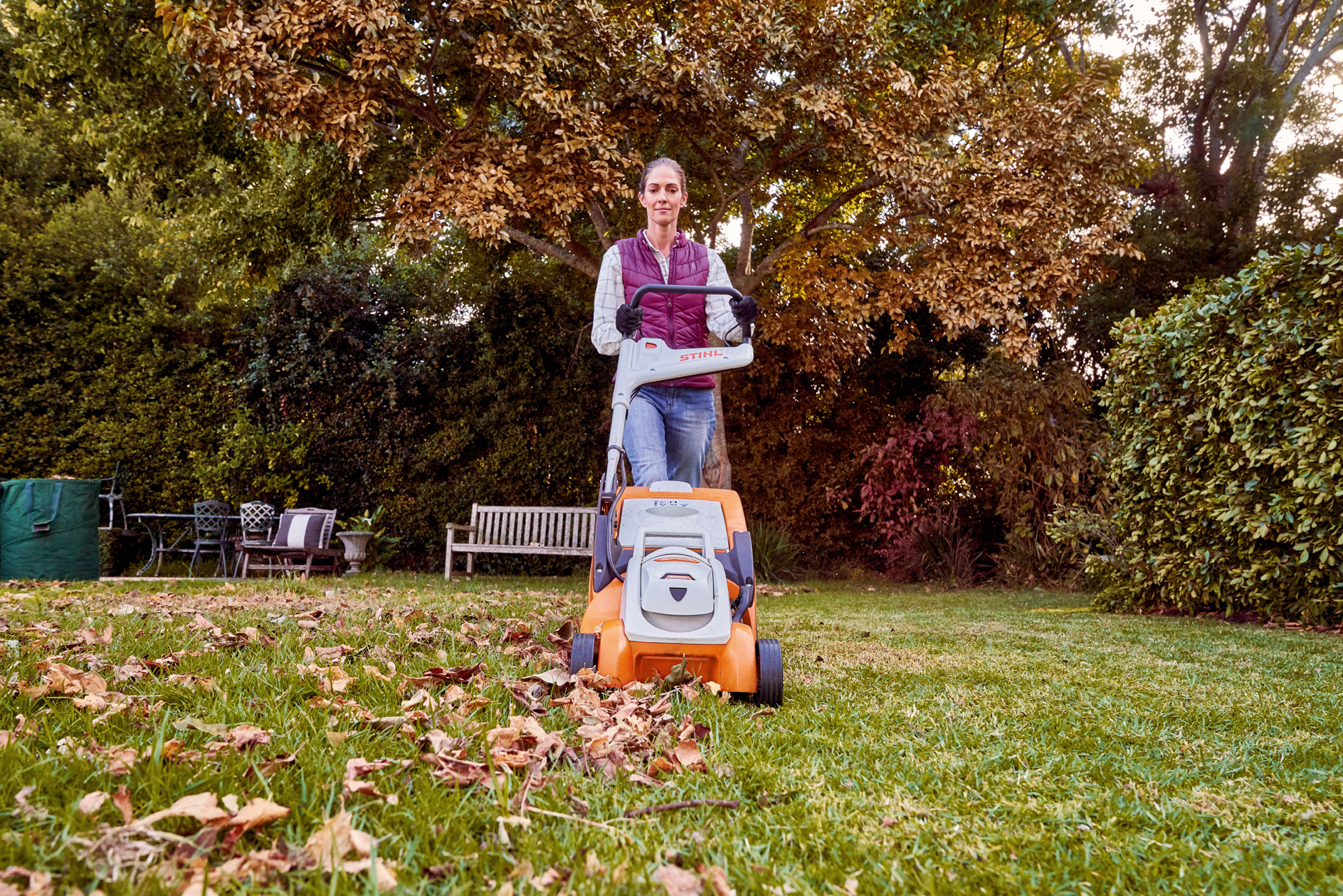 Woman using STIHL RMA 339 C battery-powered lawnmower in a garden for lawn care in autumn