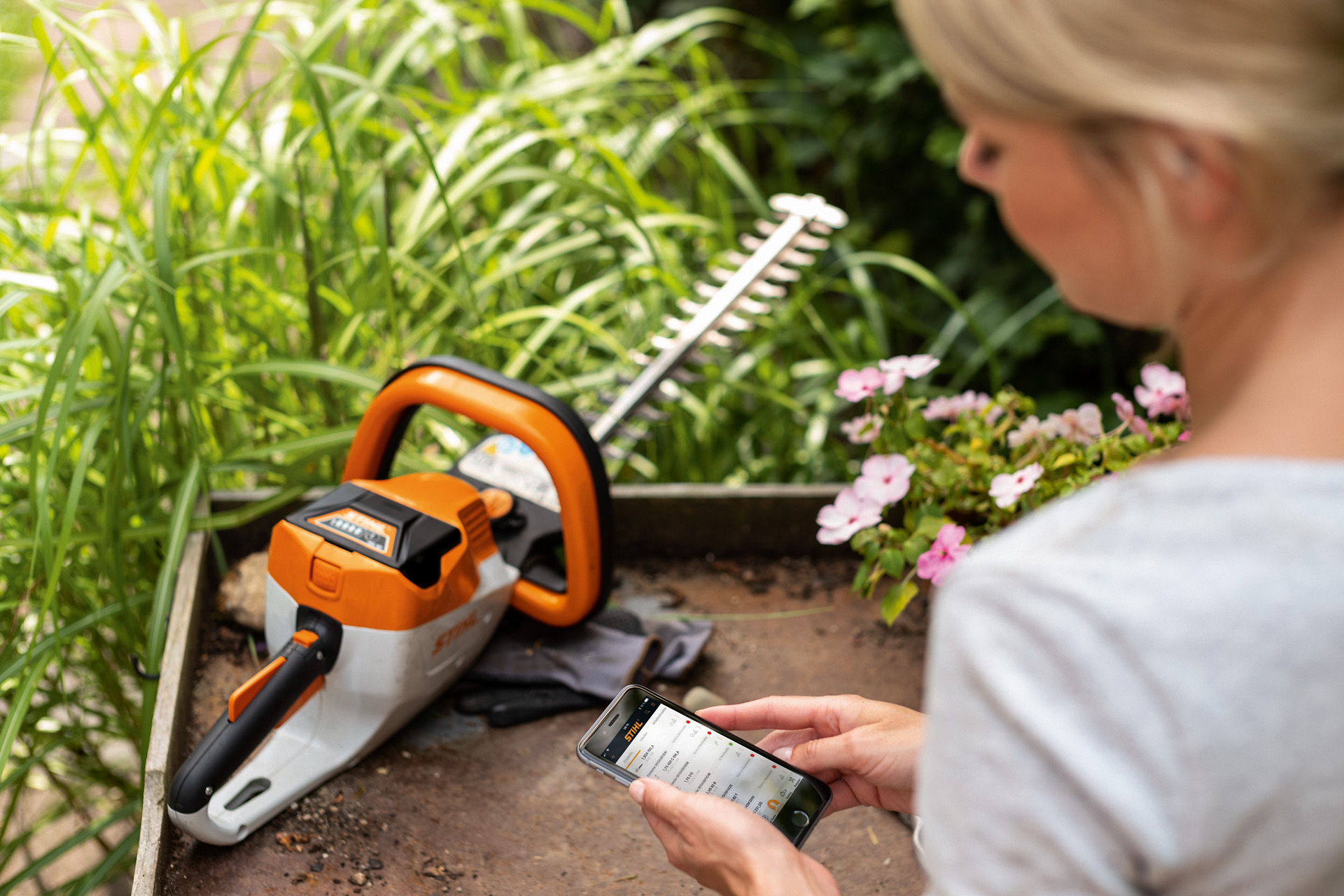 Une femme enregistre son taille-haie STIHL avec l’application STIHL sur un smartphone