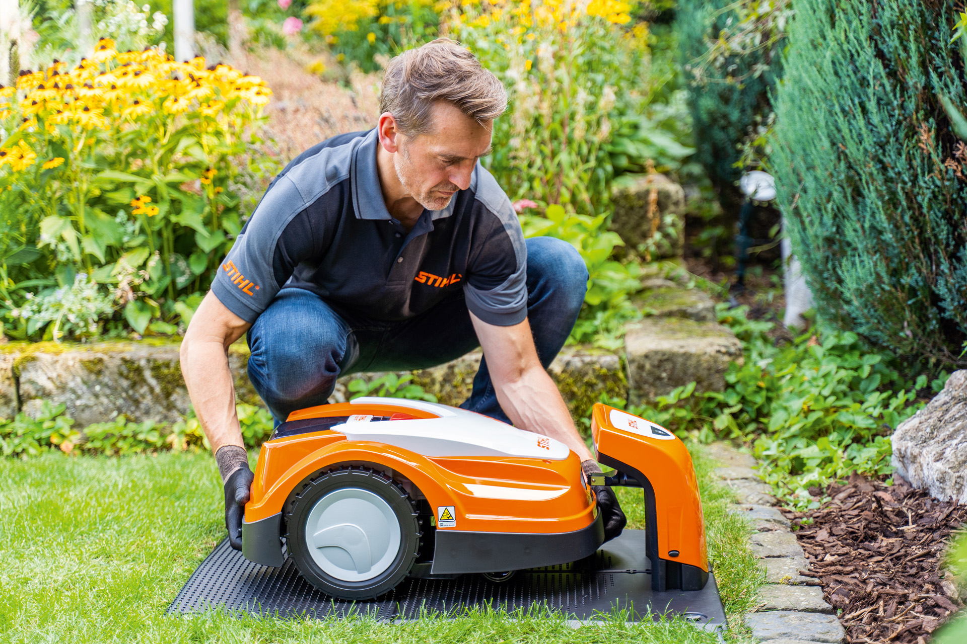 A STIHL dealer places a STIHL iMOW robotic mower in its charging station in a garden