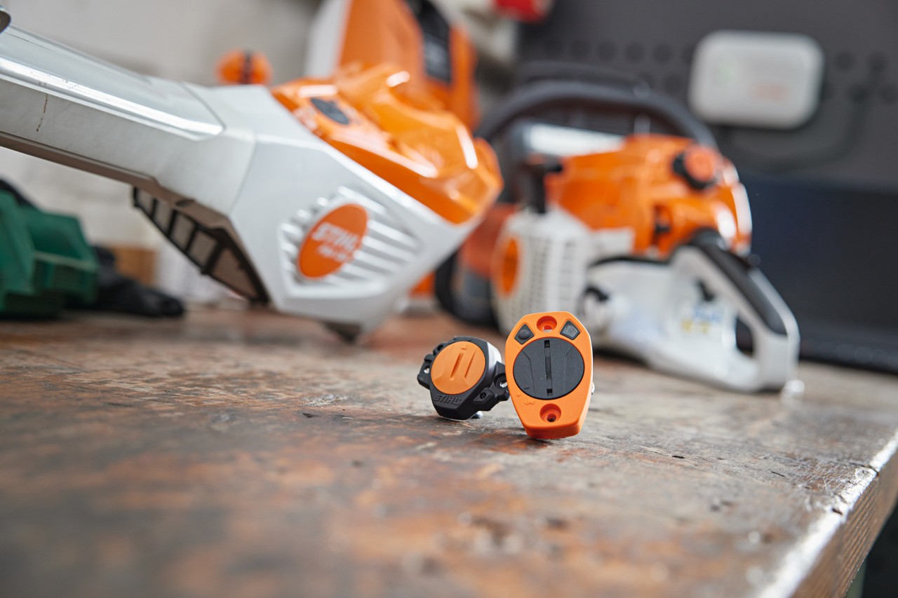 A STIHL Smart Connector and a STIHL Smart Connector 2 A on a workbench. Various STIHL tools can be seen out of focus in the background.