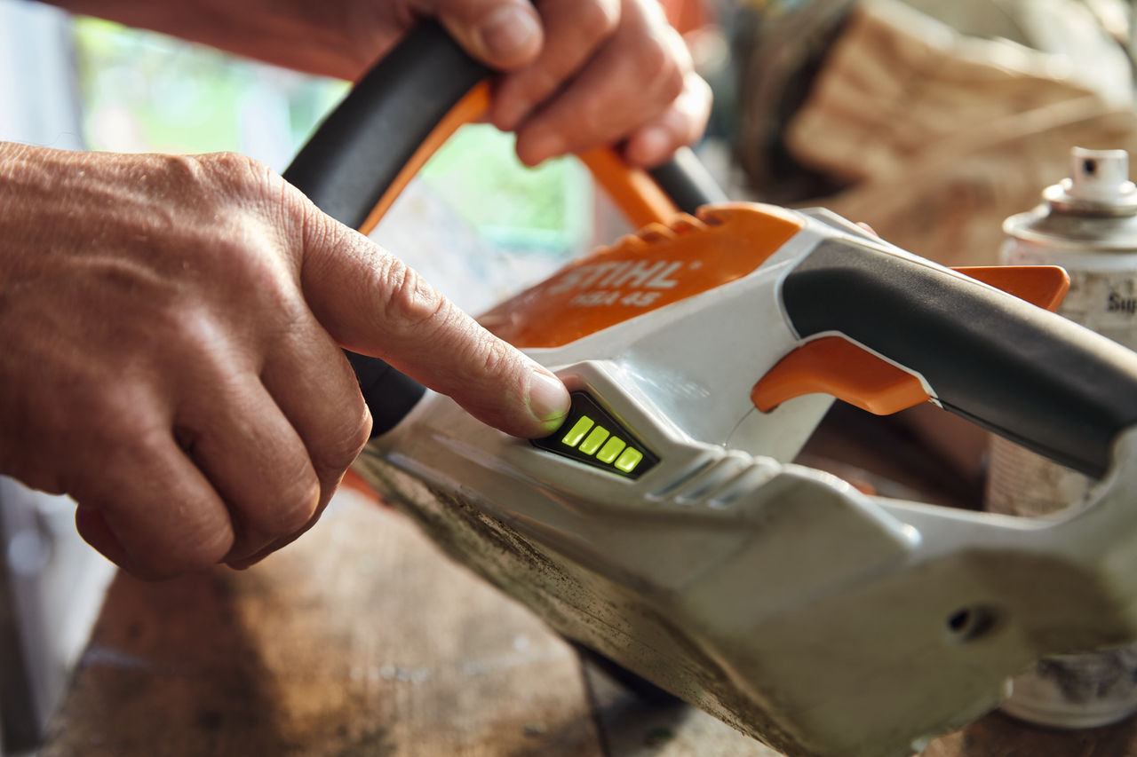 A person checks the charge level of the STIHL HSA 45 cordless hedge trimmer.