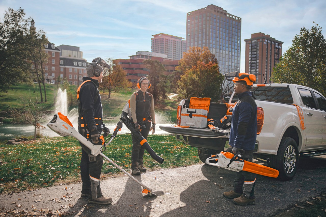 A group of professional landscapers standing around their vehicles and getting ready for work with STIHL cordless tools.