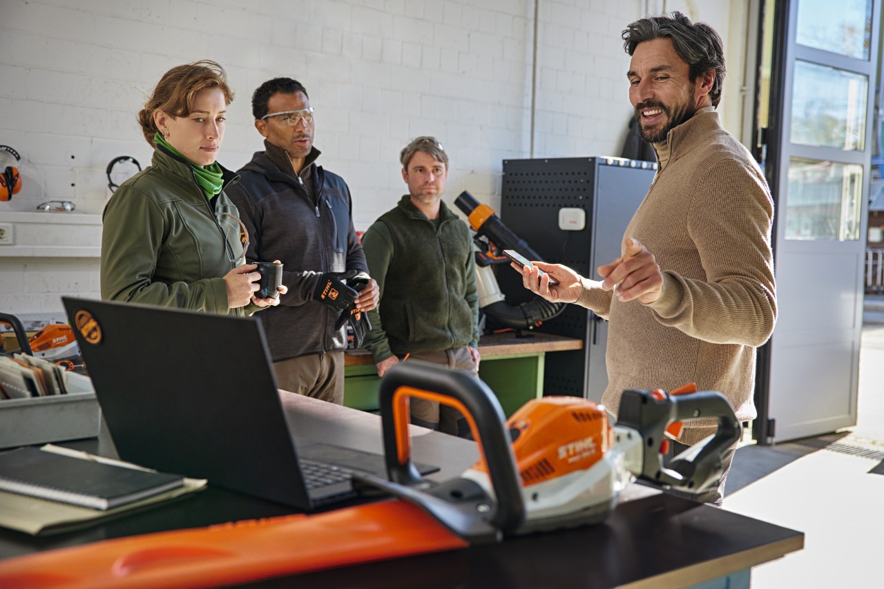 Une équipe de paysagistes discute de son travail dans un entrepôt à l'aide de l'application STIHL connected sur son smartphone.