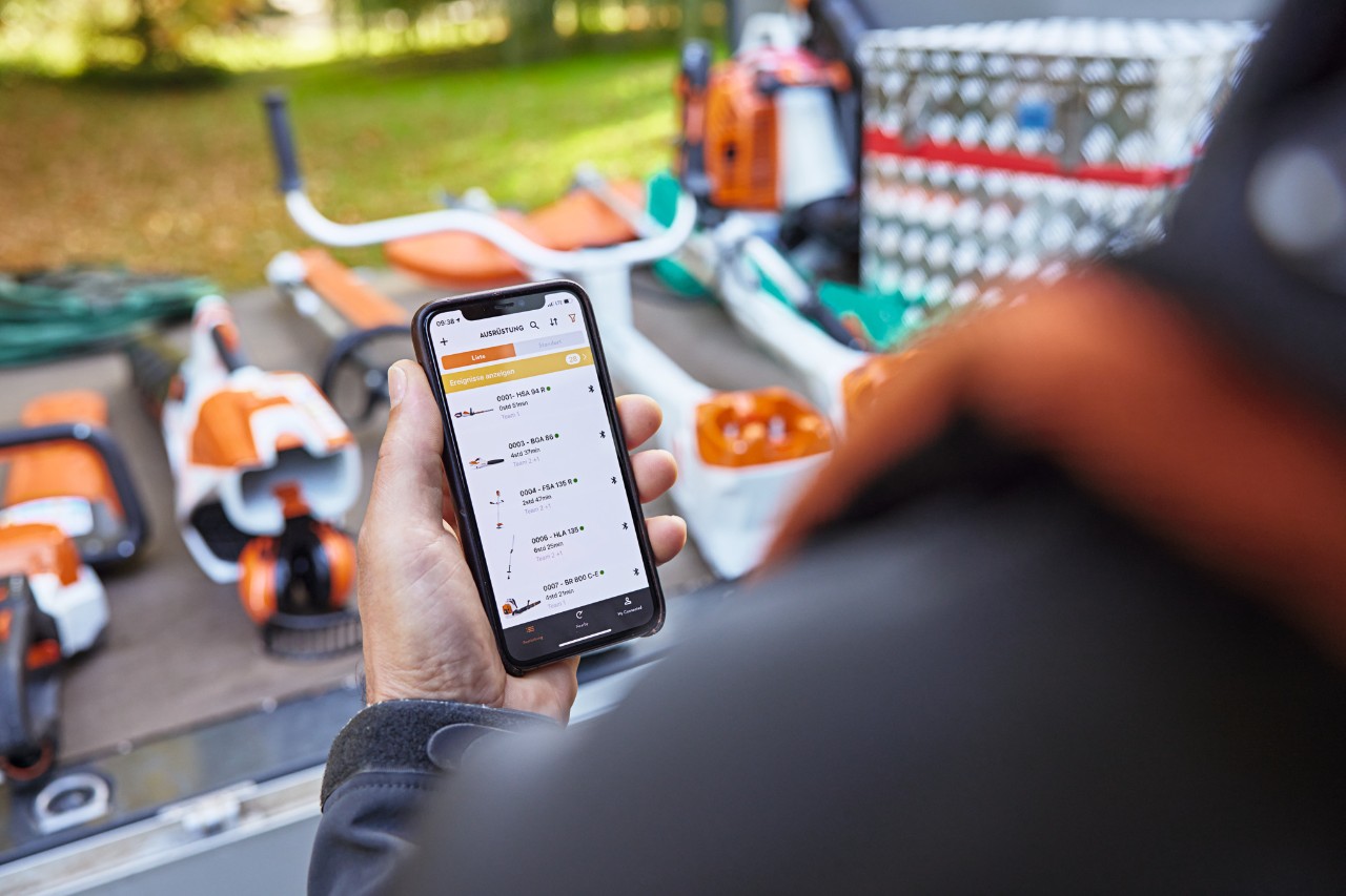 Quelqu’un se tient devant la surface de chargement d’un véhicule à plateau sur lequel sont placés divers appareils STIHL. La personne tient dans sa main un smartphone sur lequel la STIHL&nbsp;connected&nbsp;App est ouverte. 