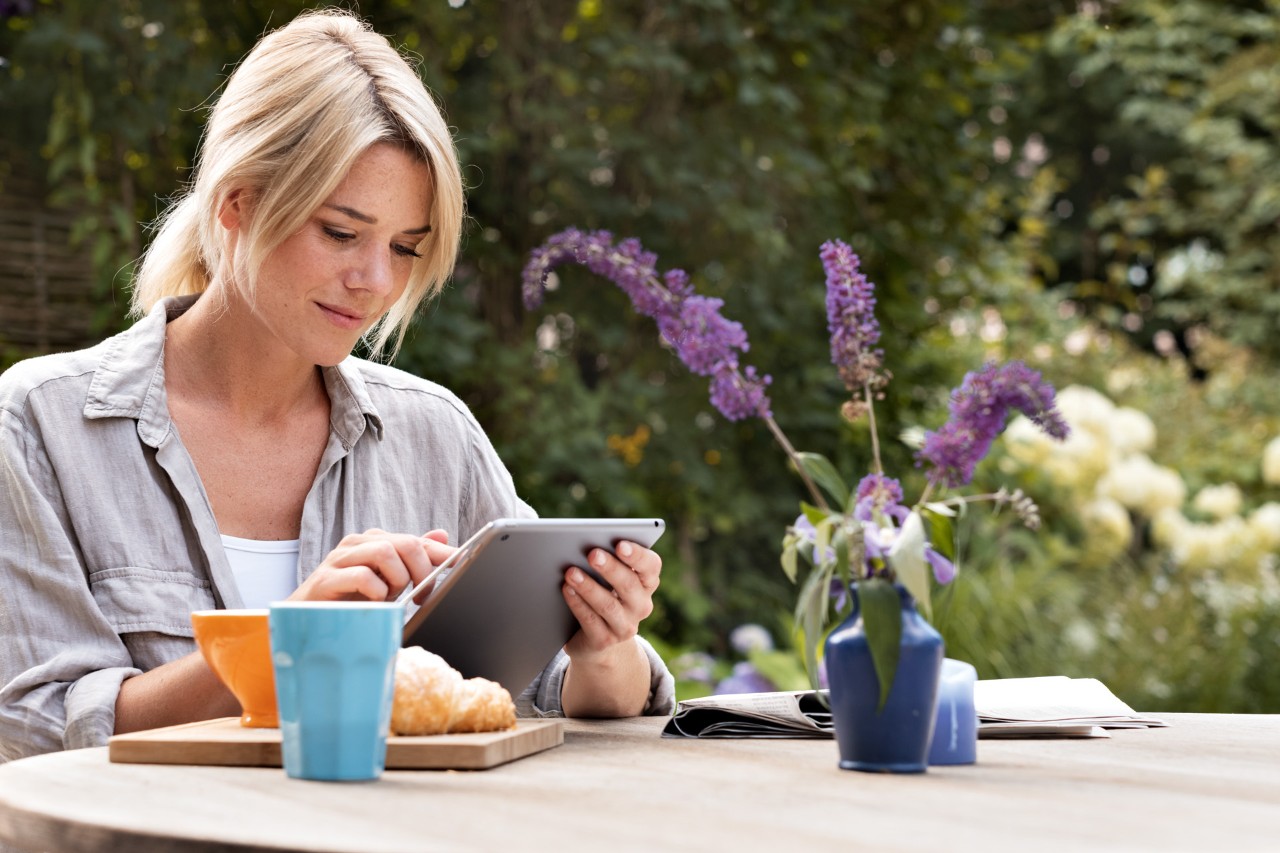 Femme utilisant une tablette assise à une table à l’extérieur pour contrôler la tondeuse robot iMOW